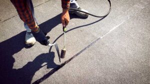 Homeowner inspecting damaged shingles and flashing beside a ladder after a rainstorm.